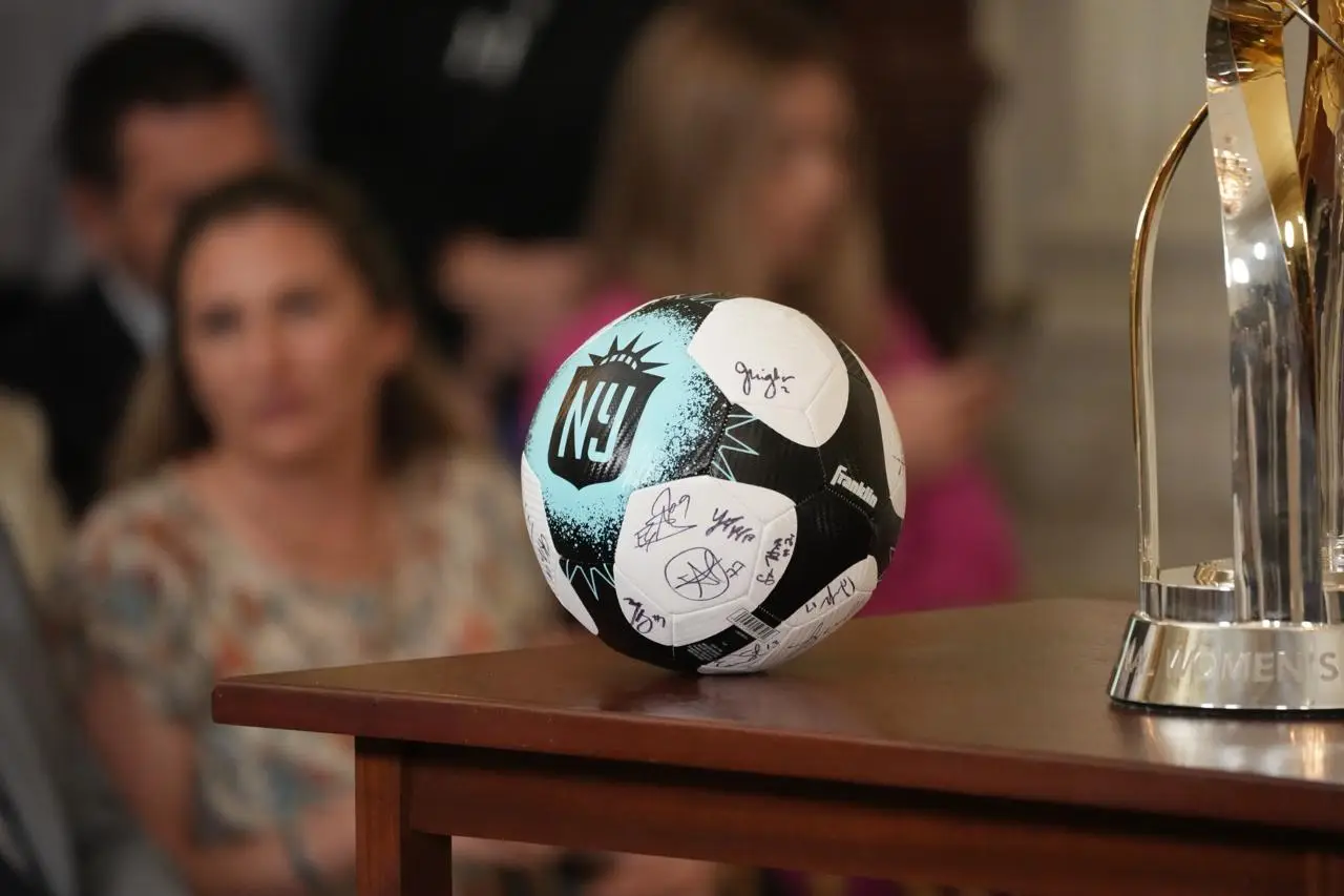 Signed Gotham FC soccer ball beside the NWSL Championship trophy