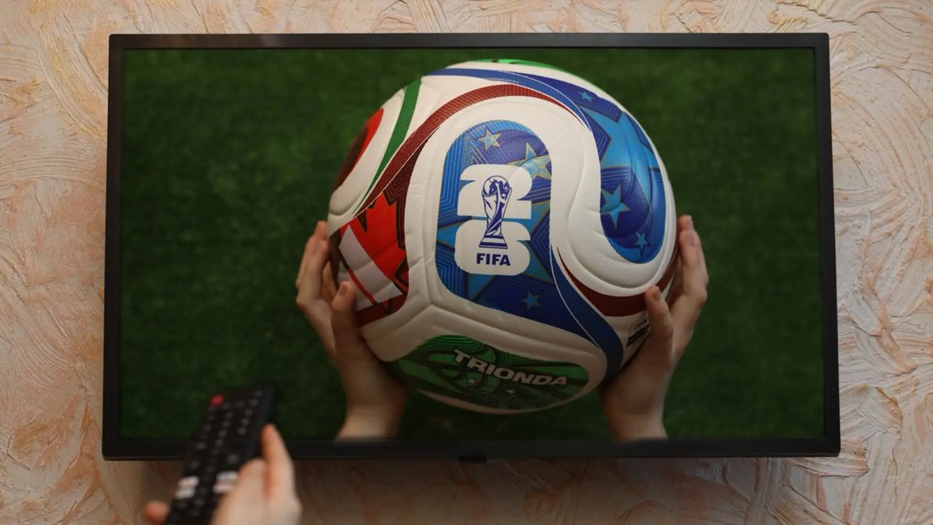 World Cup ball shown on a television screen as a viewer holds a remote control