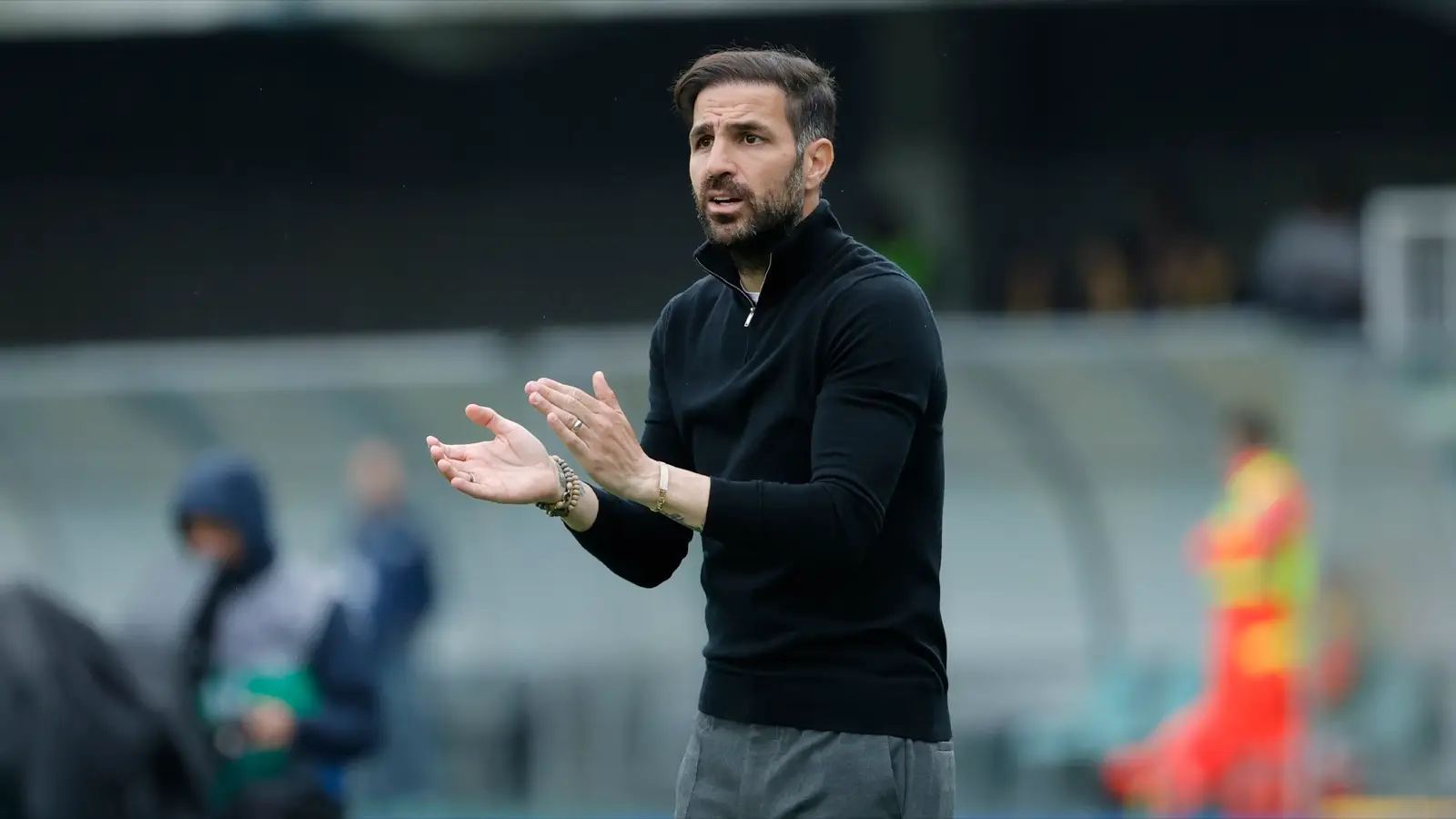 Cesc Fàbregas coaching Como from the touchline in a black knit top and gray trousers.