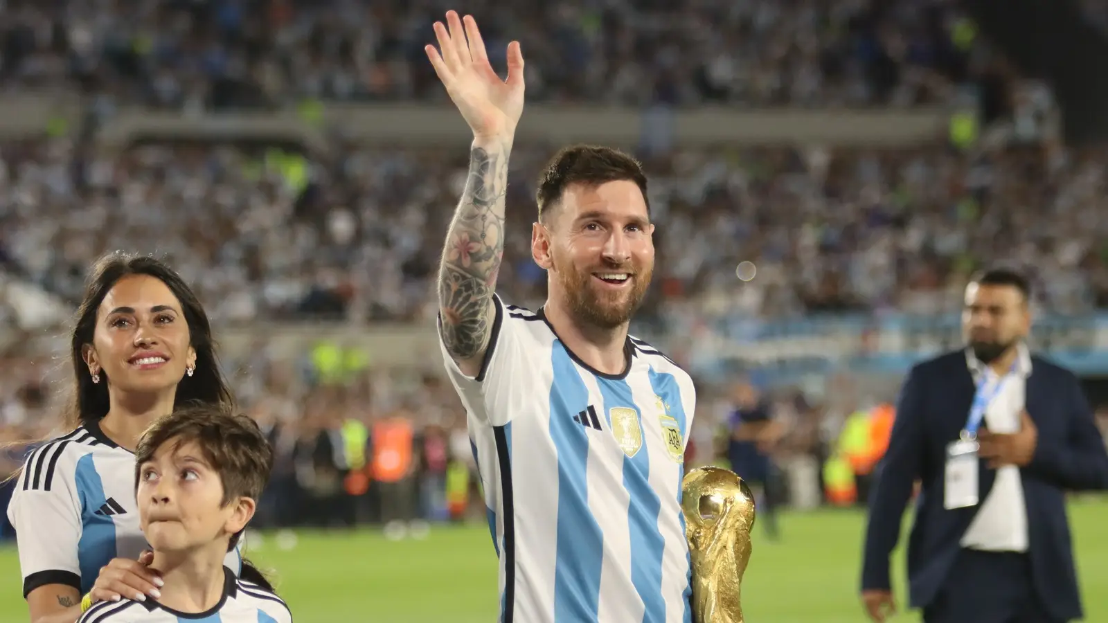 Lionel Messi waves while holding the World Cup trophy in an Argentina shirt