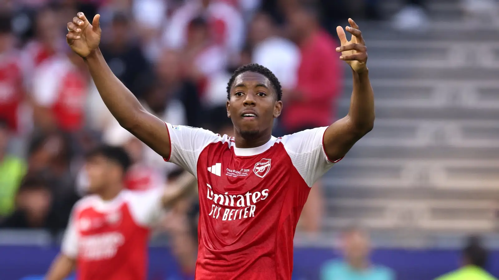 Myles Lewis-Skelly raises both arms while playing for Arsenal