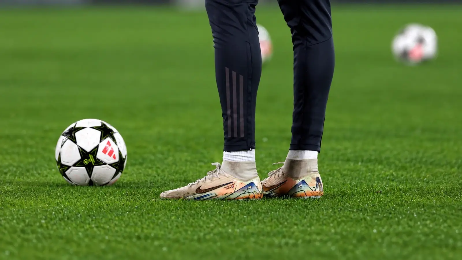 Close-up of gold Nike football boots beside a Champions League ball on the pitch.