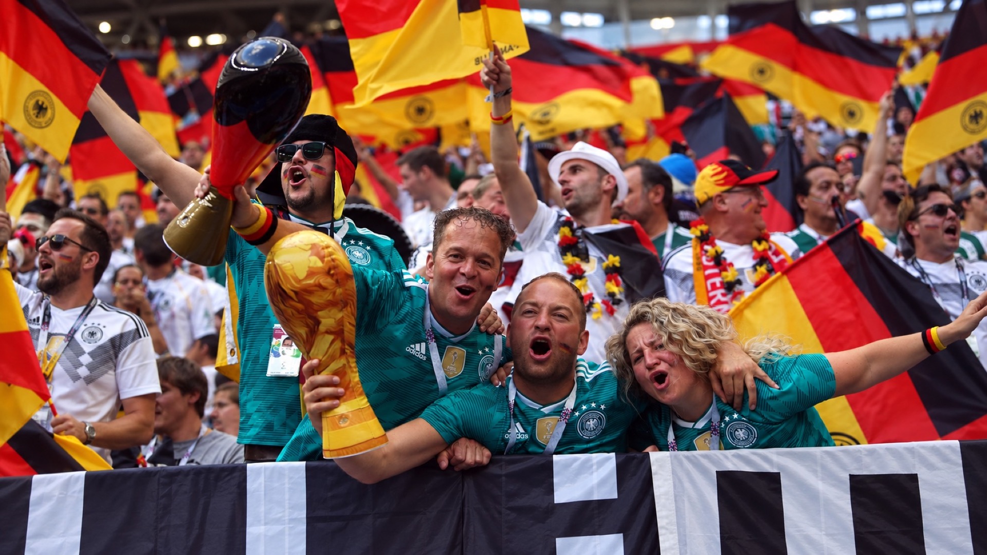 Germany supporters wearing the green 2018 away shirt, waving flags and holding an inflatable World Cup trophy.