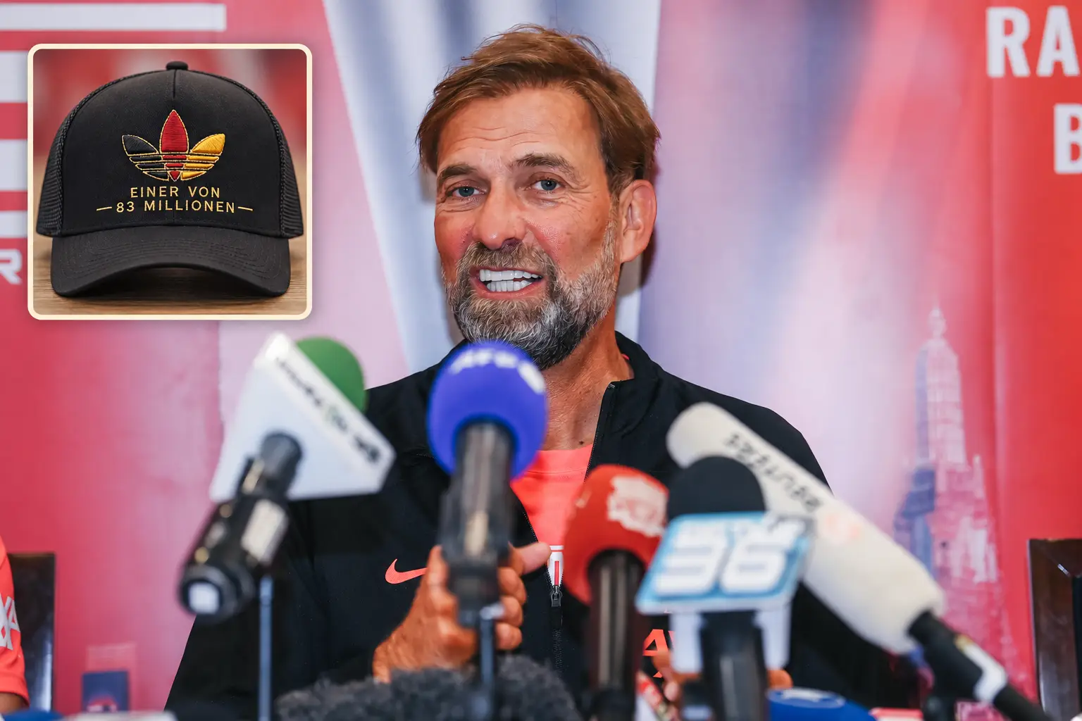 Jürgen Klopp at a press conference with an illustrated inset of the black Einer von 83 Millionen cap