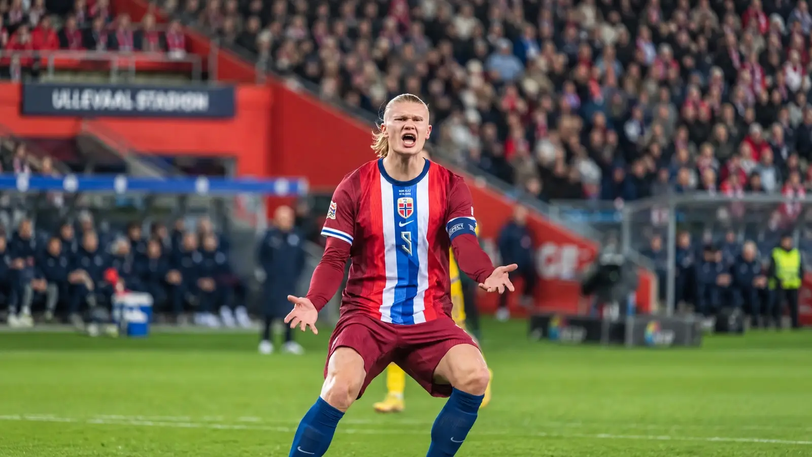 Erling Haaland in Norway’s red kit with his ponytail tied back and both hands outstretched.
