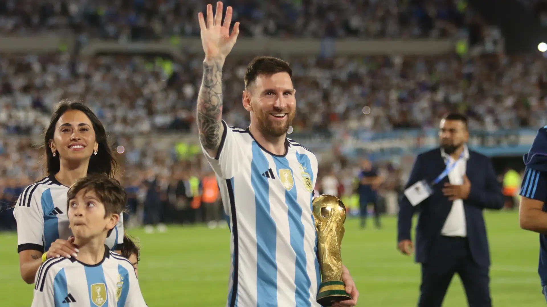 Lionel Messi waves to Argentina supporters while holding the World Cup trophy beside his family.